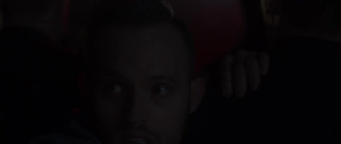 Man looking concerned as he moves through a thick crowd with flashing lights all around