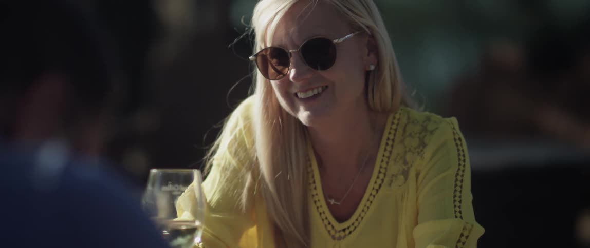 A woman sitting at a table with a wine glass smiles and laughs