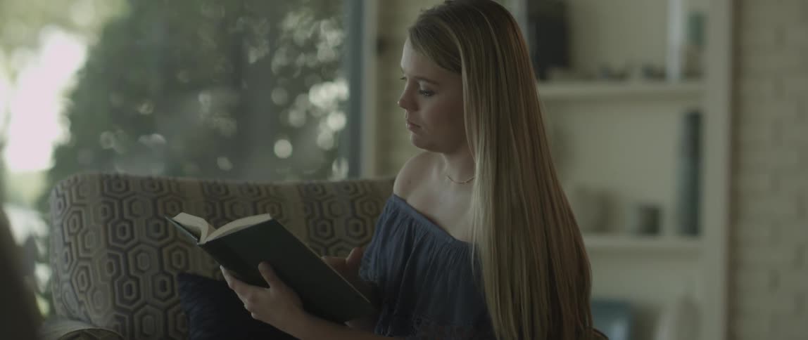 Woman sitting on chair in living room reading a book during the day