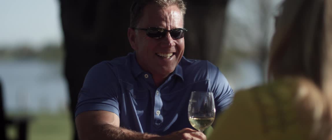 A man holding a wine glass laughs as he sits outside with a woman