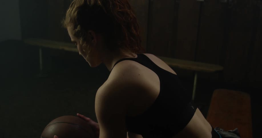 A female athlete holds a ball in her hands as she sits in a locker room