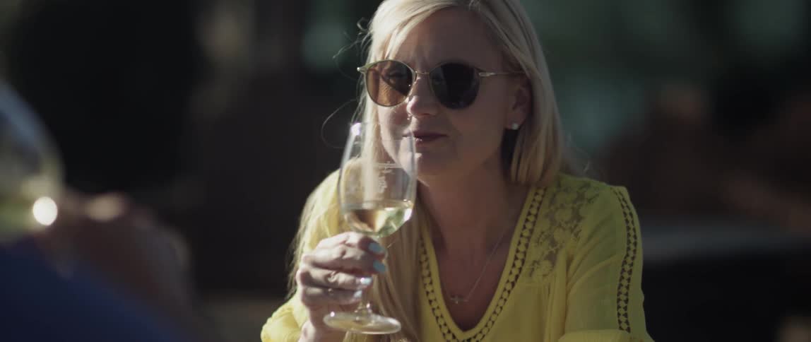 A woman drinks wine after toasting with a companion