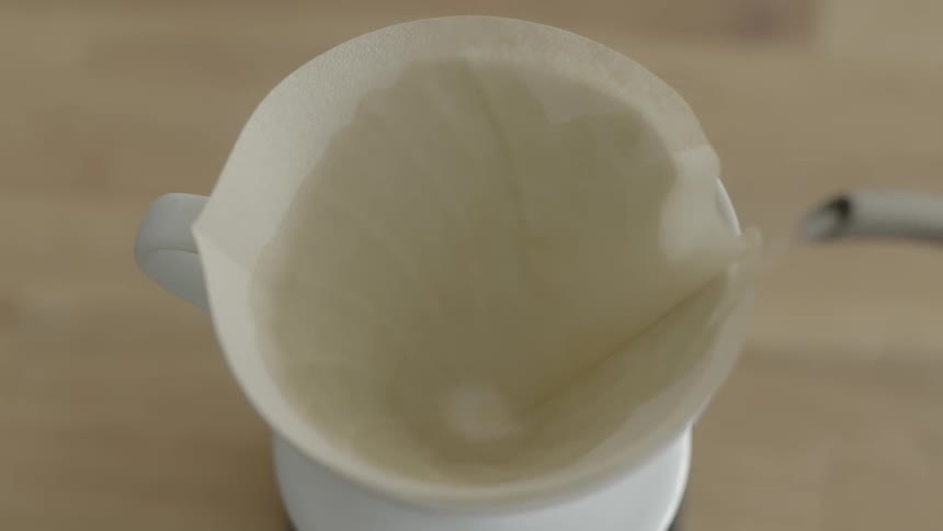 Hot water is being poured into a cup containing a white filter