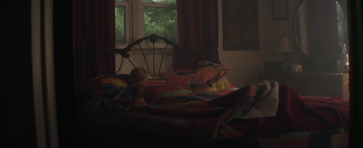 An elderly man lays in bed with a quilt