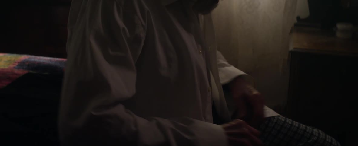Elderly man sitting on bed struggling to button shirt
