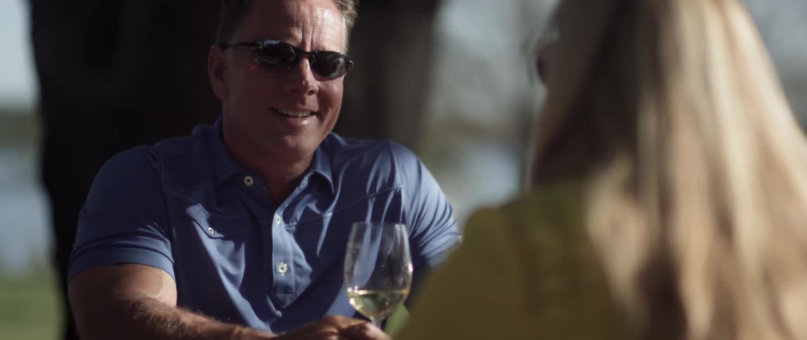 A man holding a wine glass is talking with a woman at a table