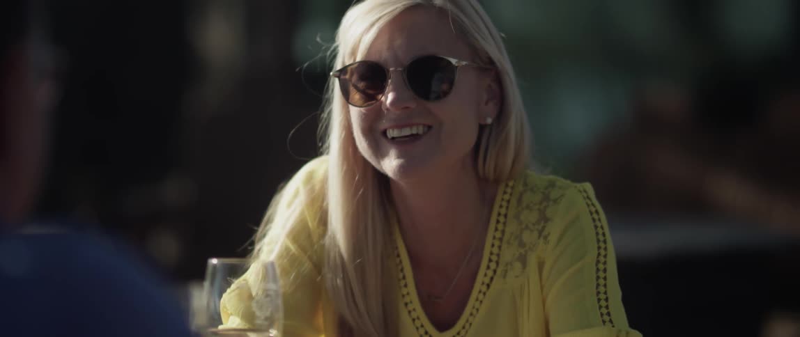 A woman laughs and smiles while drinking wine outside