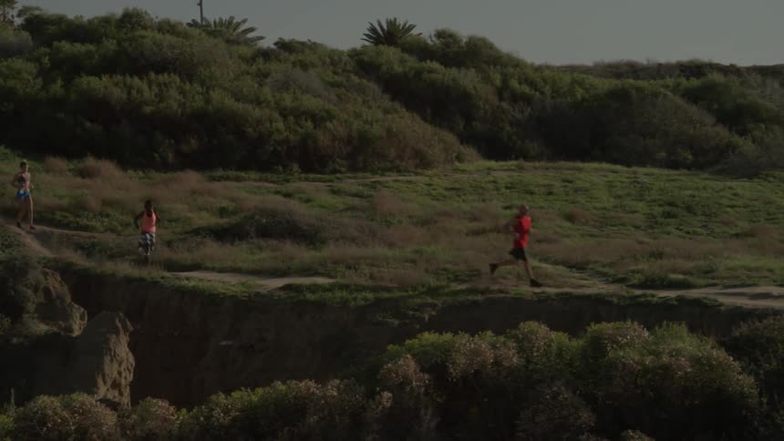 Three people race down the hills in the grass