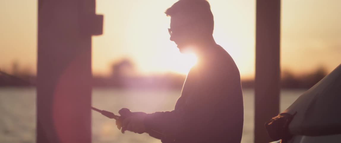 A man is fishing off a pier at sunset