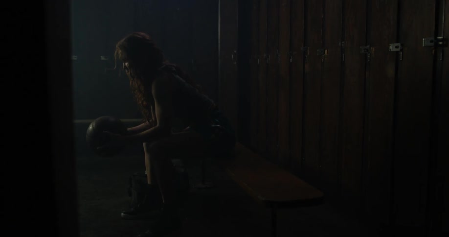 A woman is leaning forward in a locker room holding a ball