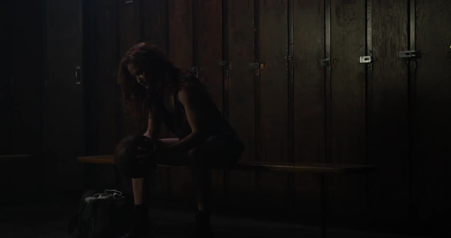 A lady is sitting in a locker room holding a basketball