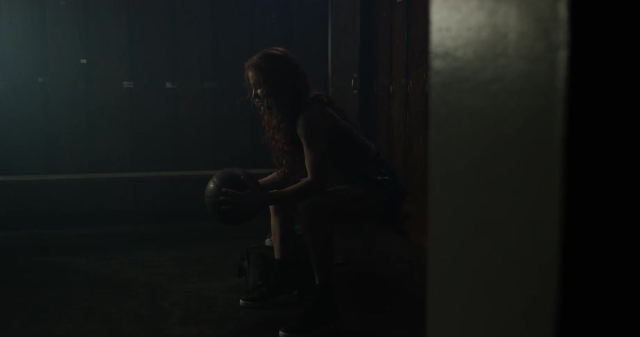 A woman sits in a locker room holding a basketball
