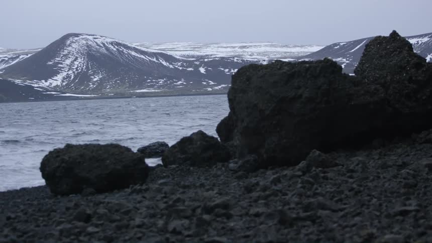 A shore that is across from a snowy mountain and separating the areas is a river