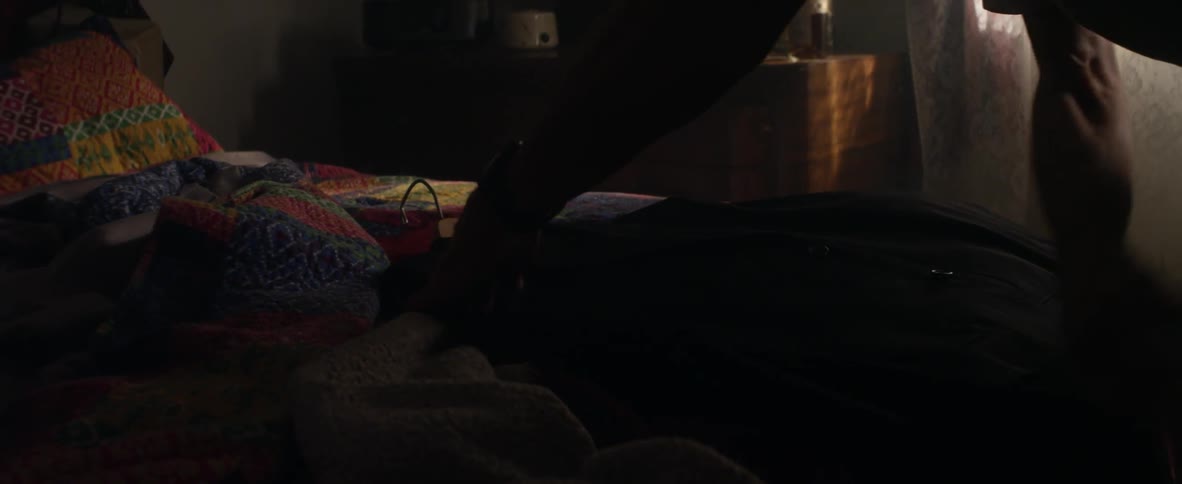 An elderly man wipes off a jacket laying on a bed