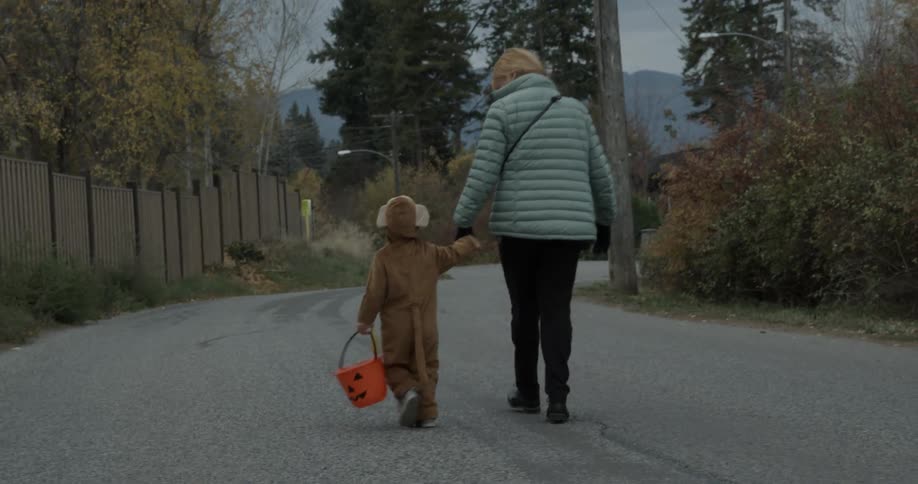 A woman walks a young child to trick or treat