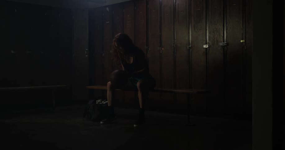 A woman is bouncing a basketball as she sits in a locker room