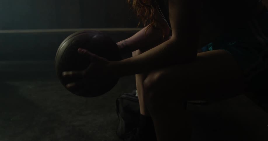 A woman holds a basketball while sitting in a locker room