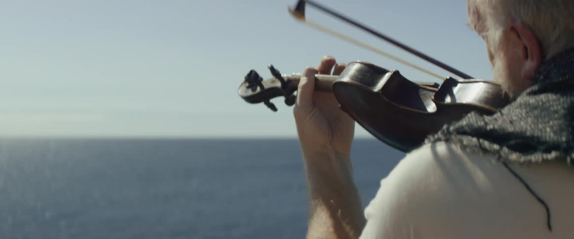 A man is playing the violin while looking out at the sea