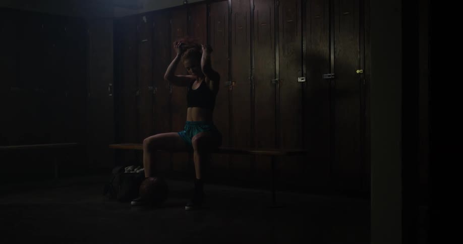 A woman removes her top and puts her hair in a ponytail before picking up a basketball