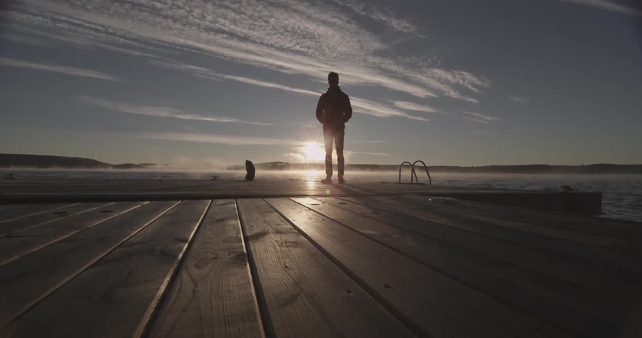 A man stands on a dock and looks out over a body of water