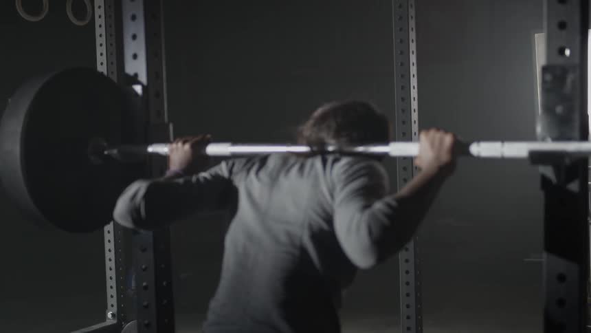 A woman is setting a bar with weights back onto a stand
