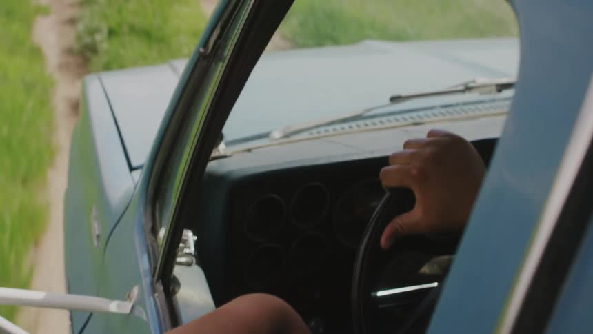 A man drives a truck on a grassy dirt road