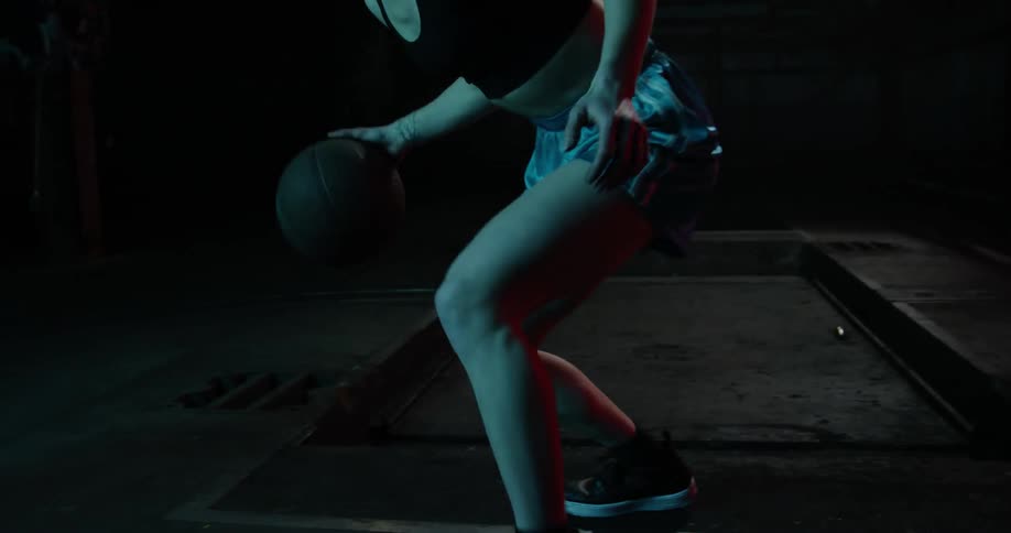 A woman dribbles a basketball at night