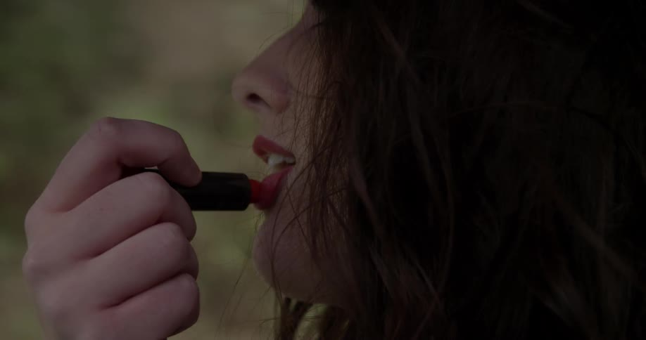 A woman applies red lipstick in the car