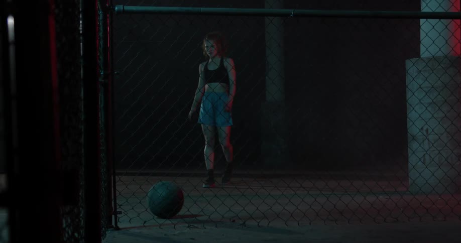 A lady kicks a basketball towards a chain link fence