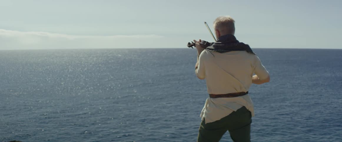 A man plays violin while overlooking the ocean