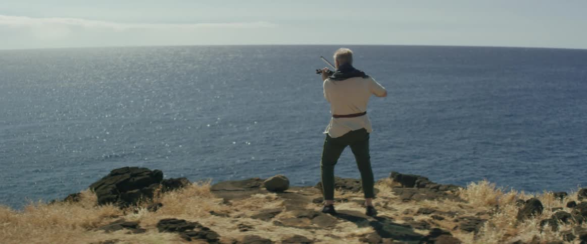 A man plays a violin overlooking an ocean