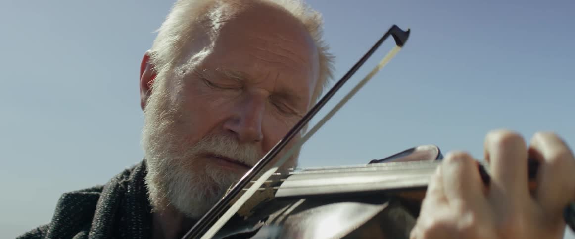 A bearded man plays violin outdoors