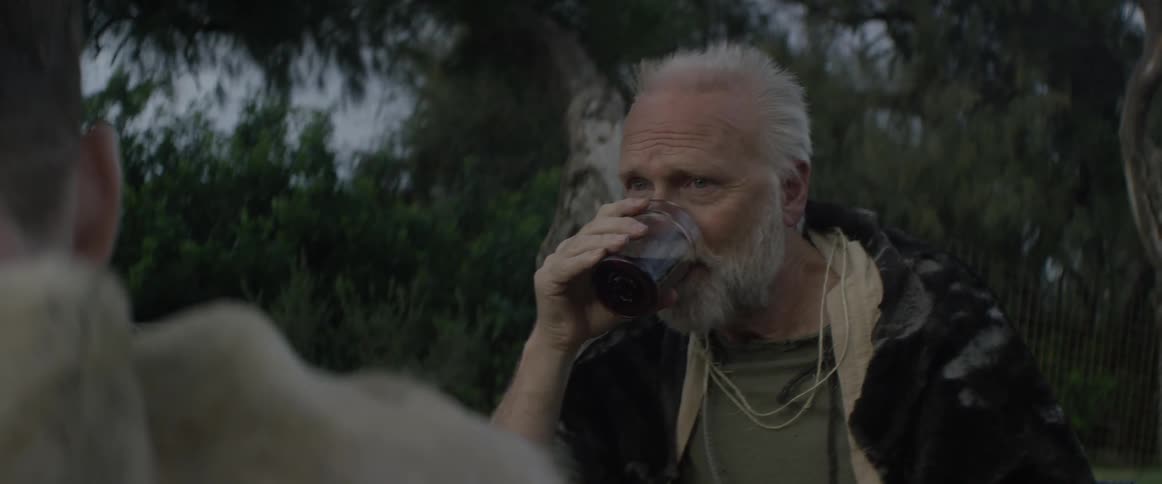 A man takes a drink while talking with a friend