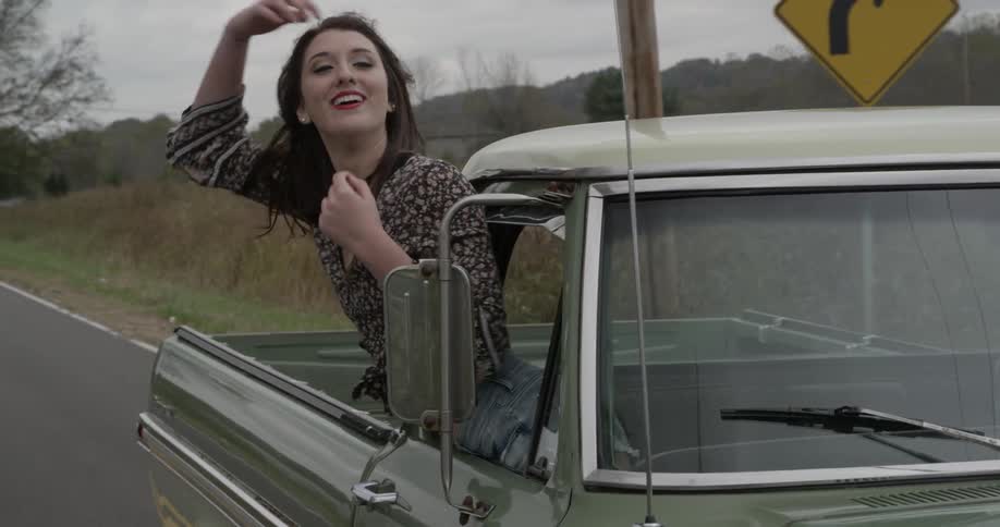 A woman leans out the passenger window of a moving pickup truck