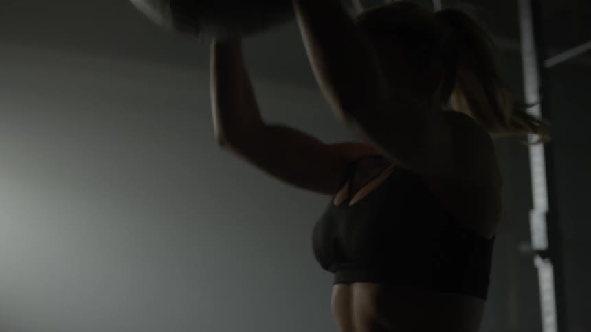 A woman lifts a medicine ball over her head then drops it to the floor