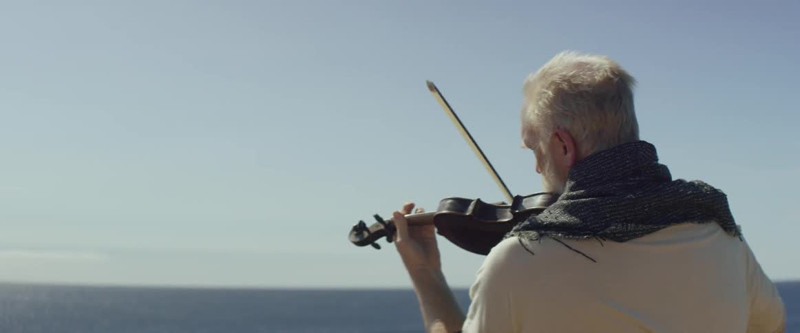 A man plays the violin while looking over the ocean