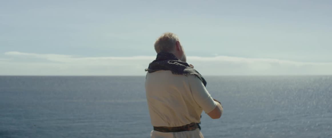 A man is playing the violin while looking at the ocean