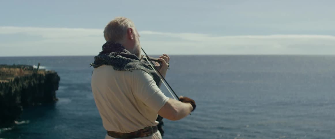 Man plays violin on a cliff overlooking water