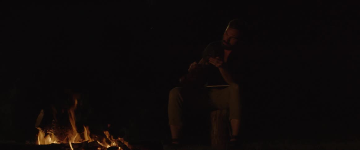 A man is holding a violin next to a fire on the ground