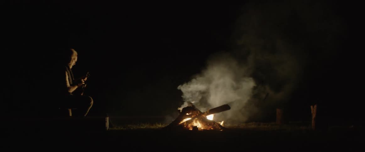 A man sits in front of a fire at night
