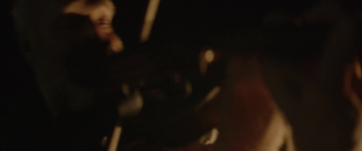 A bearded man plays the violin in a dark room