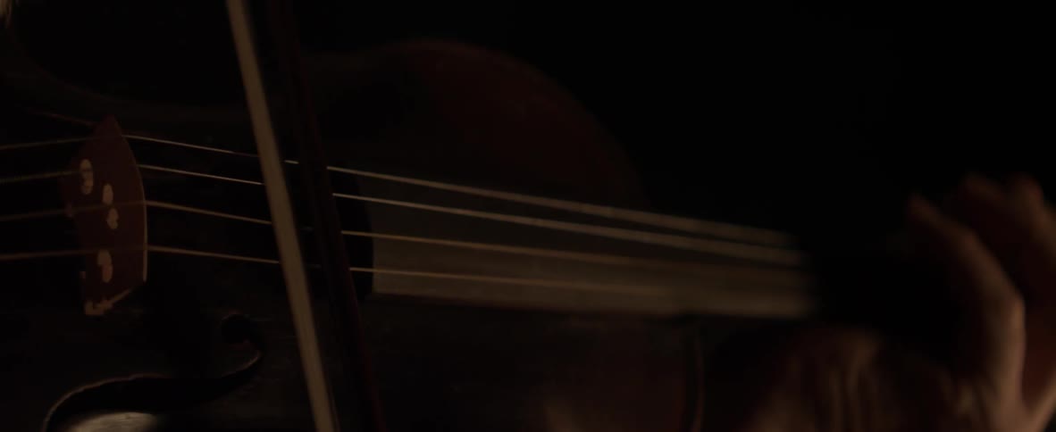 A man plays a violin in a dark environment
