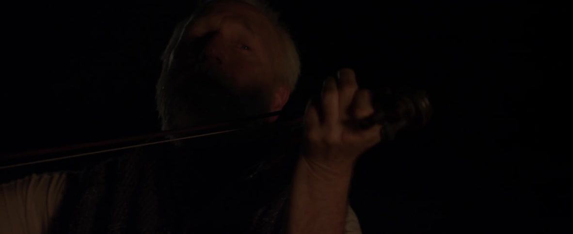 An elderly man plays violin outside in the dark