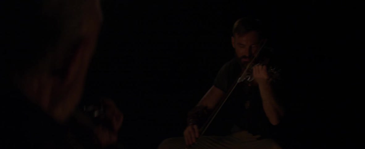 Two men play violins at night