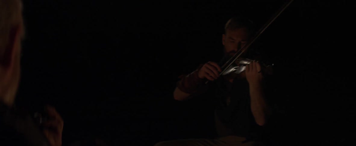 Two men sitting at a fire with violins