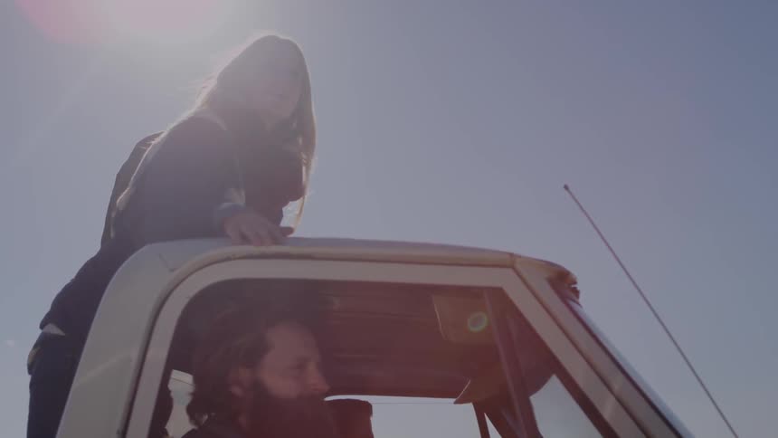 A woman stands in the back of a truck that men are riding in,