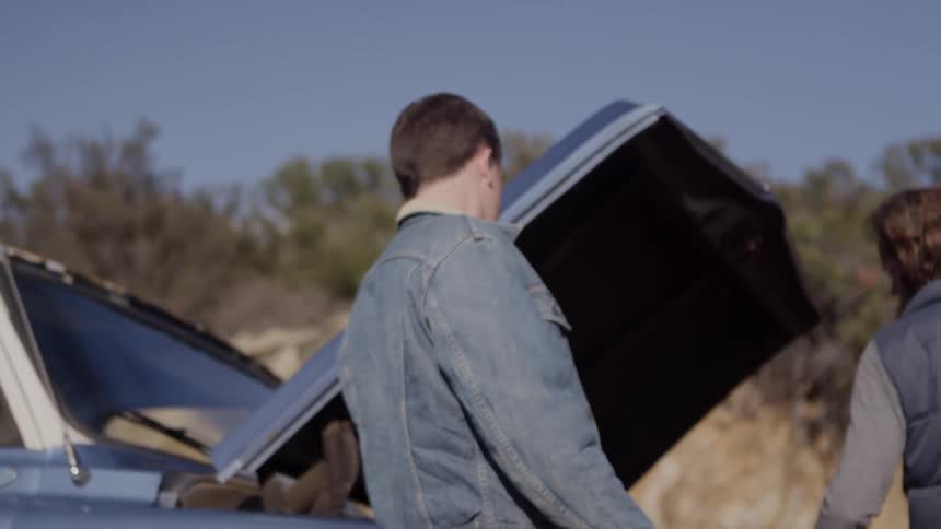 Two men and a woman stand near a blue truck on a sunny day