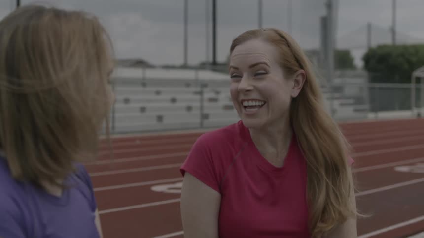 Two women at a track are talking and laughing