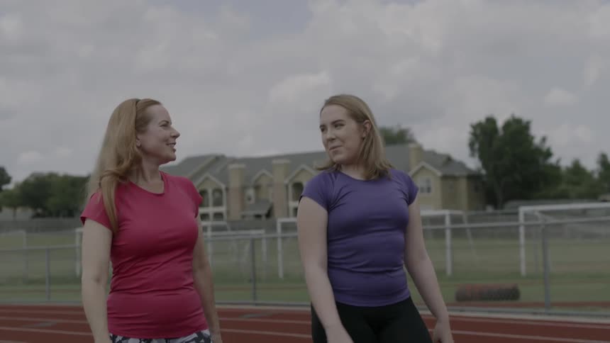 Two young women walk and talk along a running track