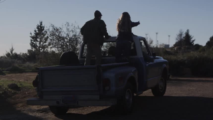 Two people ride in the back of a truck in the daytime